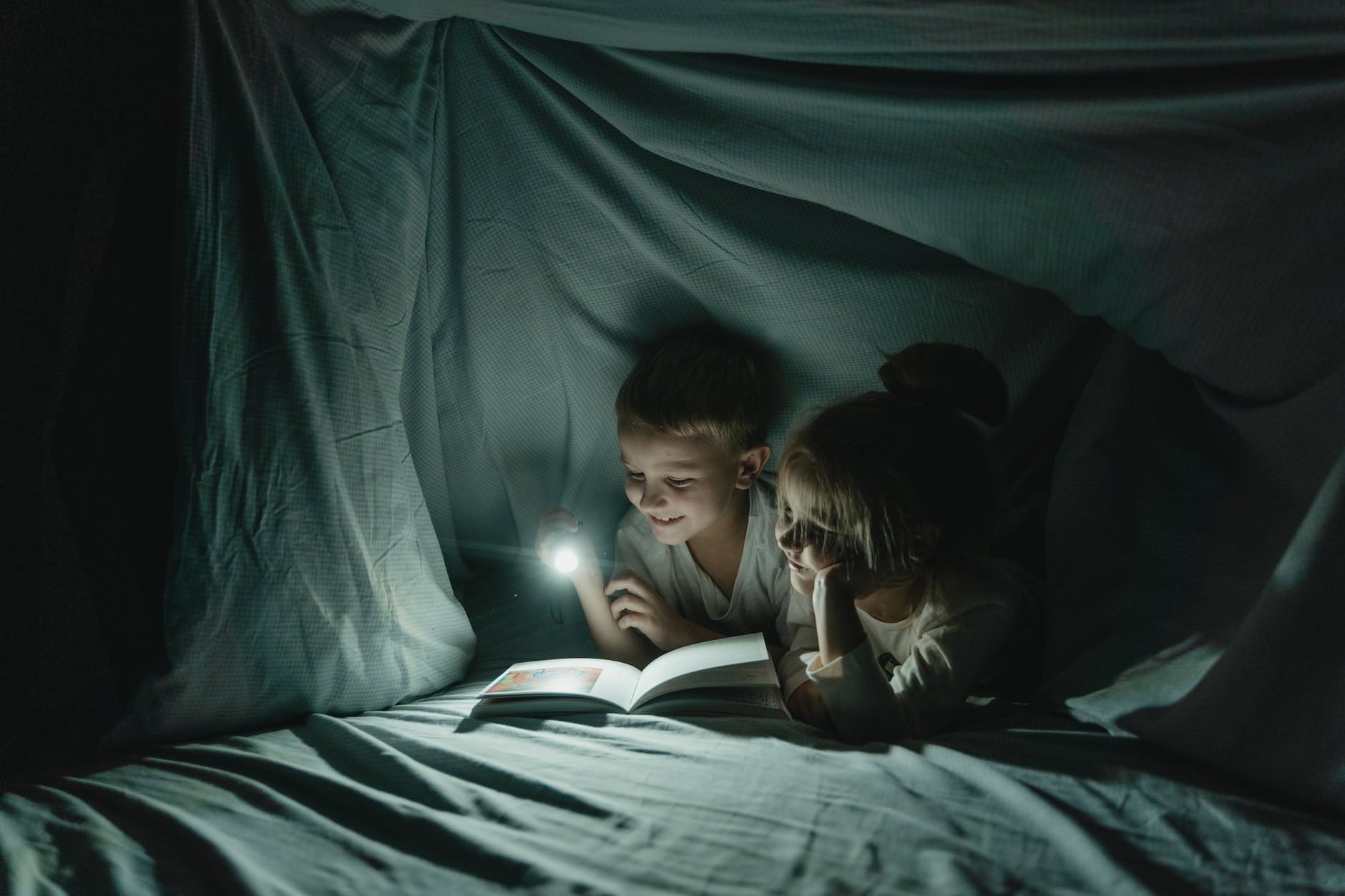 girl and boy reading book in blanket fort